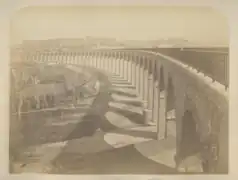 Photographie en sépia montrant le viaduc terminé, prise depuis la gauche de la balustrade de sécurité du pont qui fuit vers la gauche de l'image.