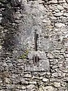 Photographie en couleurs d'un trou circulaire surmonté d'une fente verticale dans un mur en maçonnerie.