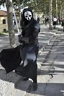 Homme habillé en noir avec un masque blanc.