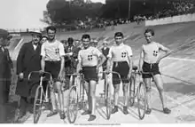 Photographie montrant les quatre cyclistes italiens debout à côté de leurs vélos dans le vélodrome.