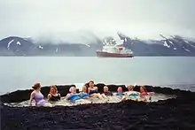 Touristes profitant des sources chaudes sur une plage de sable noir.