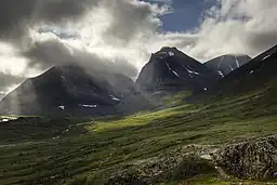 Patch de lumière sur les landes et prairies au pieds de grandes montagnes sombres.