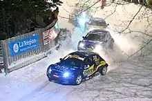 Voitures de course beues, vue de trois-quart avant prenant un virage à droite sur la neige.