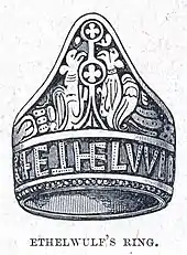 Dessin au trait d'une bague gravée de dessins et de lettres capitales.