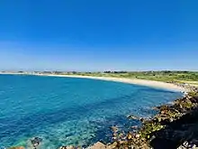 Une grande plage arrondie sépare la mer de la plaine littorale.