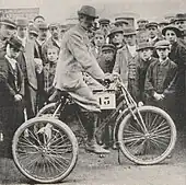 Photo d'un homme en tenue de ville sur un vélo portant un numéro à l'occasion d'une course.