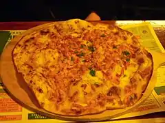 photographie d'une tarte flambée alsacienne à la crème, oignons et lardons