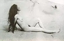 Louise Bryan de profil; nue sur une plage, se chauffant au soleil, cheveux longs non coiffés