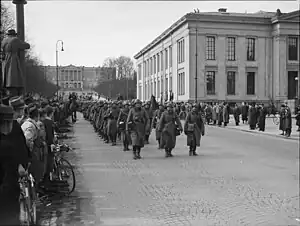Des soldats défilent dans une rue sous les yeux de la foule.