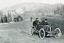 Photo d'une voiture en course, en sortie de virage sur une large route de terre.