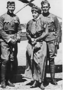 Photo noir et blanc montrant deux hommes en uniforme, de chaque côté d'une femme âgée tenant une canne.