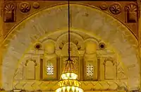 Photographie de la décoration du tympan de l'arc qui se trouve au-dessus du mihrab. Le tympan est occupé par cinq niches de différentes tailles, dont celle du milieu est la plus grande. La décoration de ce dernier inclut des carrés posés sur la pointe, des arcs à cinq lobes et des claustras garnis de verres de couleur.