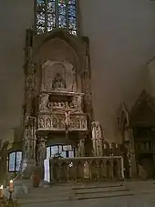 un mur d’église, percé d’ouvertures grillagées, devant lequel se trouve un tombeau monumental et un autel