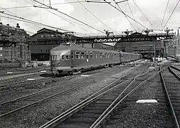 Départ d'un long train d'Amsterdam-Central comportant une rame quadruple et une remorque postale.