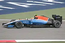 Photographie d'une monoplace de Formule 1 bleue et rouge, vue de profil, dans son ensemble, sur la piste.