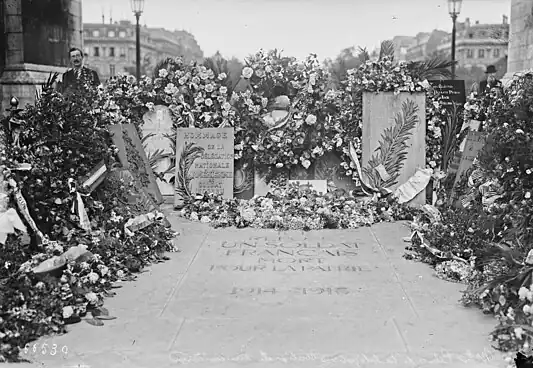 Photo en noir et blanc montrant un amoncellement de couronnes de fleur autour d'une pierre tombale