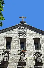 Zoom sur la partie haute d'une façade d'église en pierre avec trois niches comportant des statues de saints.