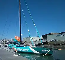 Vu de trois quarts avant, voilier à foils bleu, blanc et vert amarré au ponton.