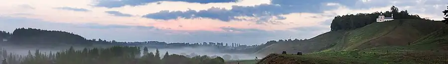 Vallée avec de la brume dominée par des collines, avec à droite l'église.