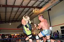 Un catcheur casse une guitare sur la tête d'un autre catcheur.