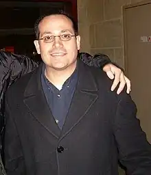Homme caucasien portant des lunettes, une chemise bleue foncée, et un manteau noir (photo prise en 2007).