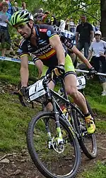 Homme descendant une pente à VTT dans une tenue noire et verte.