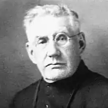 Portrait en noir et blanc d'un homme de face, aux cheveux blancs, avec des lunettes.