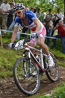Homme descendant une pente à VTT, portant une tenue bleu-blanc-rouge.