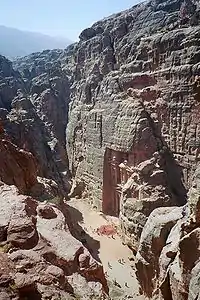 Un monument sculpté dans la roche vu d'en haut. Il y a des promeneurs qui passent dans le défilé en face du monument.