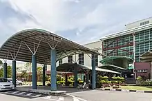 Photographie d'un grand bâtiment vitré et de ses trois portiques ombragés.