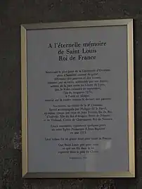 Panneau encadré posé sur un mur de pierre, et dont le titre est « À l'éternelle mémoire de Saint Louis, Roi de France »