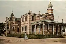 Carte postale colorée montrant un bâtiment d'inspiration mauresque, une femme se protégeant avec une ombrelle en premier plan.