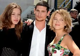 Photographie au format paysage et en couleurs de trois jeunes gens se tenant par l'épaule sur un tapis rouge.
