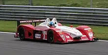 Photographie d'une voiture de sport-prototype blanche et rouge, de trois-quarts avant, sur une piste.