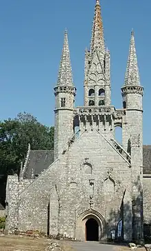 Façade dissymétrique d'une chapelle surmontée d'un clocher encadré de deux tourelles, un peu moins hautes que lui, et qui ont toutes deux une flèche, comme lui. Elles sont reliées au clocher par deux passerelles.