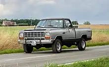 Un Dodge Ram de couleur grise roulant sur la route. Il y a deux personnes dans le véhicule, qui porte une plaque d'immatriculation allemande.