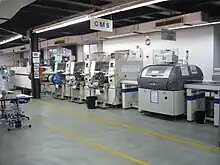 Ligne de pose de composants CMS. A droite l'équipement de sérigraphie, puis 3 stations de pose et à gauche au fond le four de refusion.