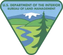 Logo dessiné triangulaire, la pointe en bas, mais aux pointes arrondies, représentant une montagne au sommet enneigé, deux monts verdoyants et une rivière descendant dans la plaine, un sapin à droite au premier plan.