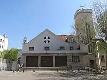 Église du XXe&nbsp;siècle. Clocher une tour octogonale sur le côté surmontée d'une croix domine un parvis.
