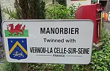 Photo d'un panneau blanc portant une inscription en anglais illustrée avec le drapeau gallois et le blason de Vernou-la-Celle-sur-Seine