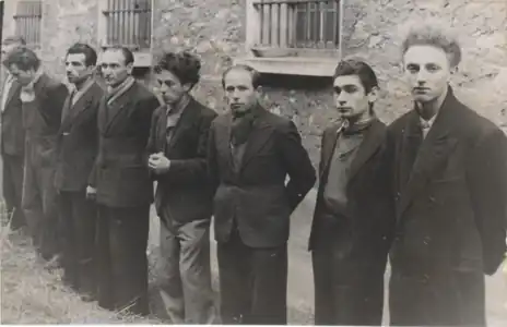 Photographie en noir et blanc d'un groupe de huit hommes réuni à l'extérieur d'un bâtiment.