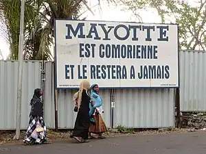 La devise sous l'écu, « Ra Hachiri » (« Nous sommes vigilants ») vient des revendications des Comores sur Mayotte (ici sur un panneau à Moroni).