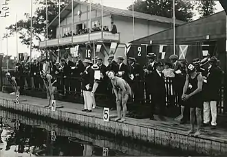 Photographie noir et blanc : quatre hommes au bord d'un bassin s'apprêtant à plonger