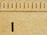 Photographie montrant une ligne de merlons arrondis, au-dessus d'une ouverture en forme de meurtrière.