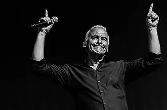 Photo en noir et blanc d'un homme levant les doigts en l'air avec un micro dans la main droite.