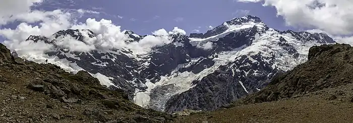Une grande montagne enneigée caressée de quelques nuages. Un glacier en descend.
