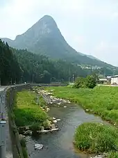 Photo couleur d'un cours d'eau avec en arrière-plan une montagne sous un ciel bleu et nuageux.