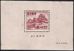 Photo couleur d'un Bloc-feuillet de couleur chair présentant, en son centre, un timbre aux teintes framboise figurant un château fort.