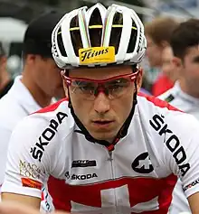 Homme portant un casque blanc, des lunettes rouges et un maillot blanc avec un drapeau suisse sur le devant.