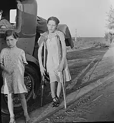 Enfants de réfugiés de la sécheresse de l'Oklahoma sur l'autoroute près de Bakersfield, en Californie. Famille de six&nbsp;personnes&nbsp;; pas d'abri, pas de nourriture, pas d'argent et presque pas d'essence. L'enfant a une tuberculose osseuse. Juin 1935.